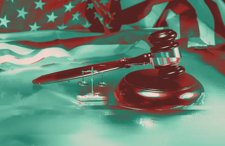 Gavel and scales of justice in front of a US flag lit in blue and purple